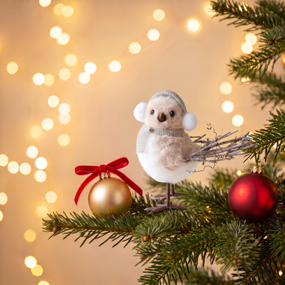 Weisser Weihnachtsvogel mit Ohrenwärmer auf einem Tannenzweig